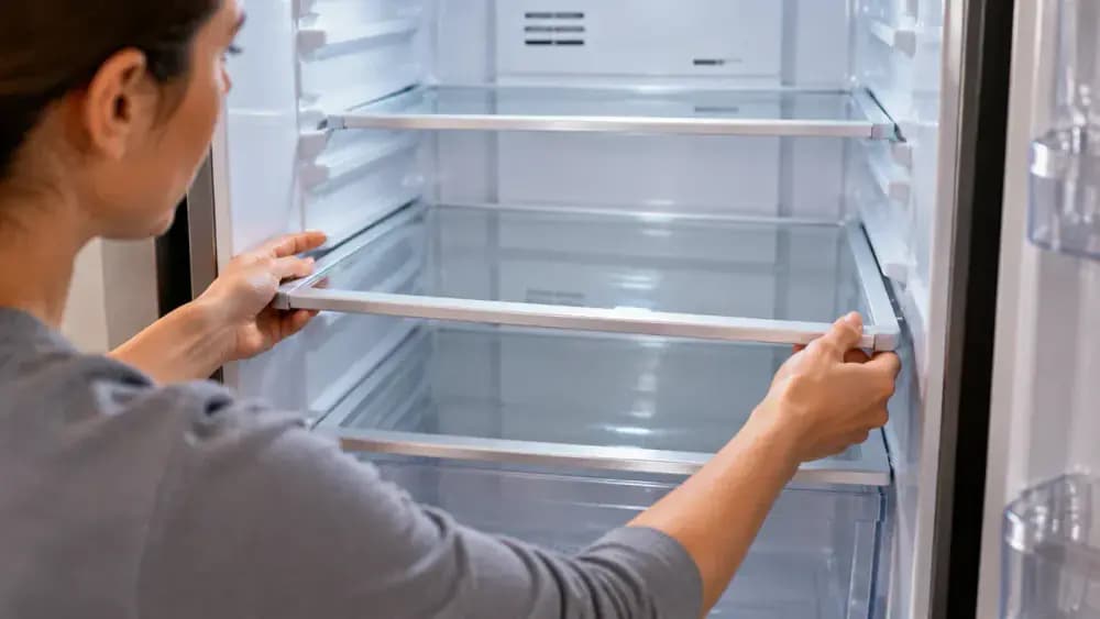 Person placing a clean refrigerator shelf back onto the side supports inside an organized refrigerator compartment