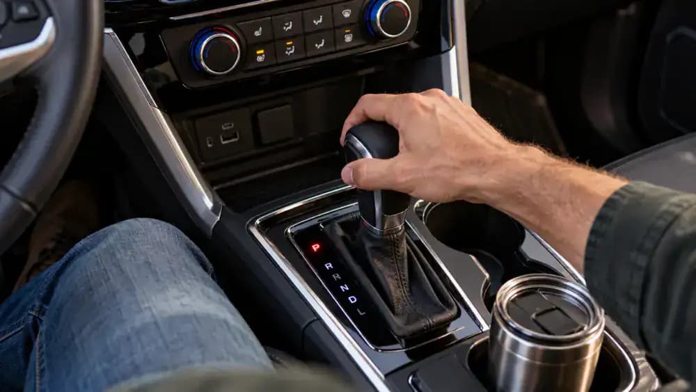 Driver checking the automatic gear selector and illuminated Park indicator in a stationary American SUV while keeping a foot on the brake.