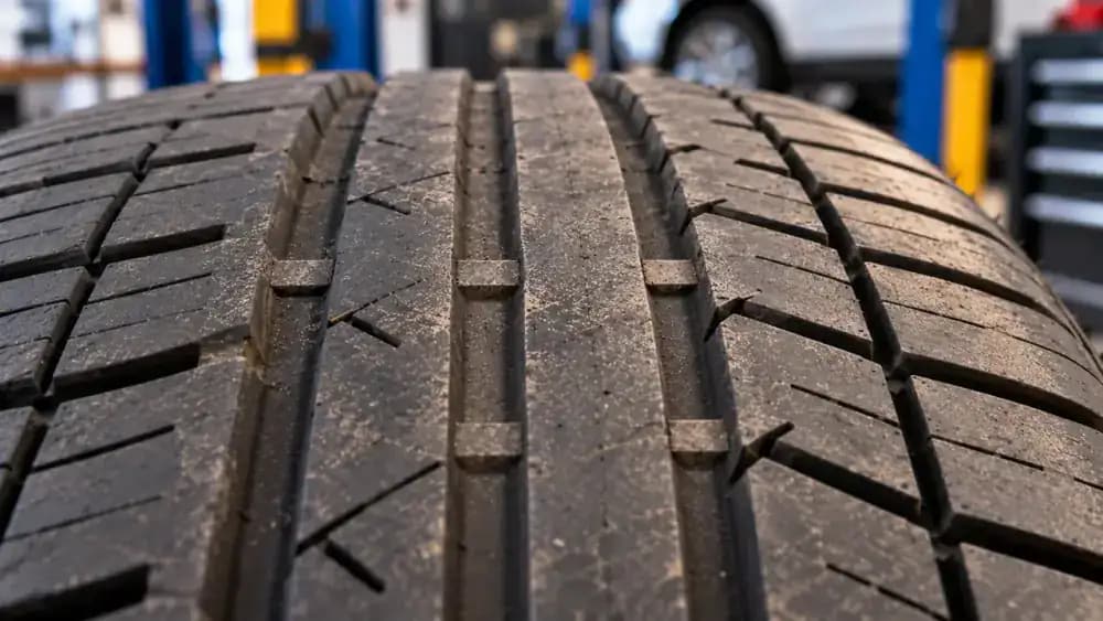 Close-up of a tire tread groove showing a raised rubber wear indicator bar, alongside an educational cross-section illustrating the tread worn level with the indicator.