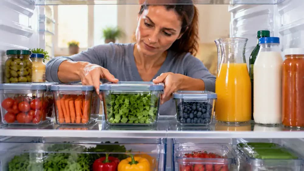 Person spacing refrigerator containers and organizing bottles upright to improve airflow and visibility on a clean shelf